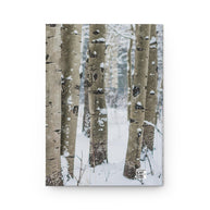 A vertical photographic print or canvas featuring a snowy winter forest with tall aspen tree trunks, shown against a plain white background.