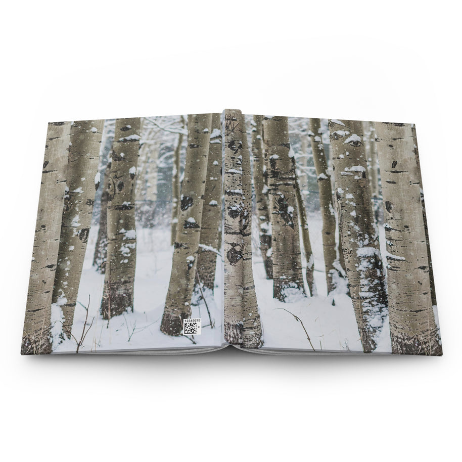 A hardcover photo book featuring a winter forest cover with birch trees and snow, shown open against a plain white background.