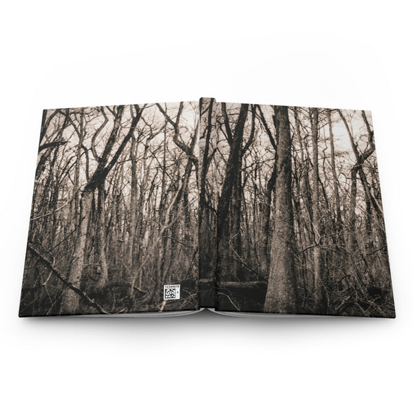 An open hardcover book displaying a sepia-toned forest photograph on both pages, photographed against a clean white background.