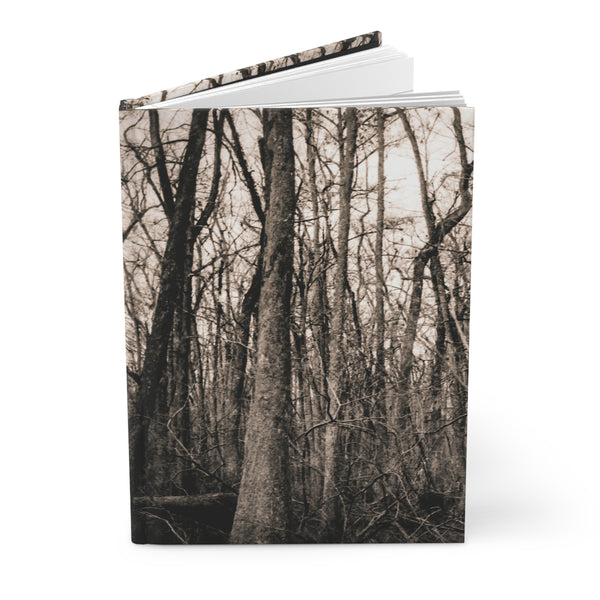 A hardcover notebook or journal standing upright, featuring a sepia-toned forest scene with bare trees on the cover. The notebook is shown open slightly at the top against a clean white background.