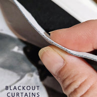 Close-up of a hand holding the edge of a black curtain panel to show its white backing, with the text 'BLACKOUT CURTAINS' in the lower left corner.