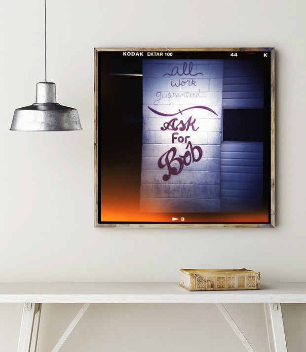 A framed bob retro photo print featuring graffiti text on a brick wall with warm orange and cool blue lighting from shop holga photography