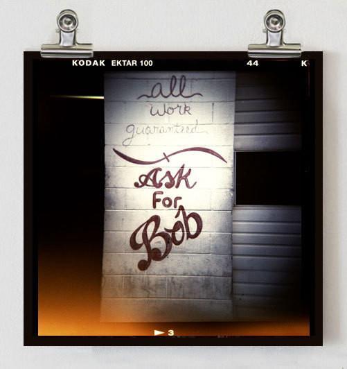 A black and white bob retro photo print with kodak ektar 100 border showing handwritten text on a brick wall, shop holga photography