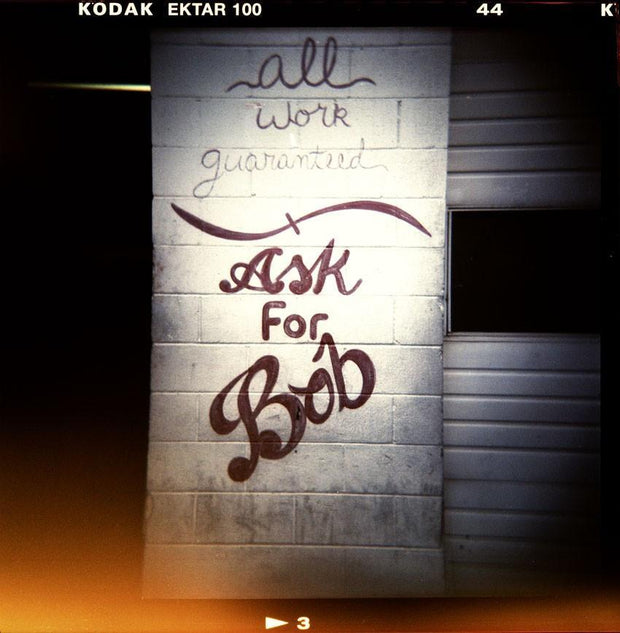 A bob retro photo print showing a weathered concrete wall with dark brown graffiti in shop holga photography style