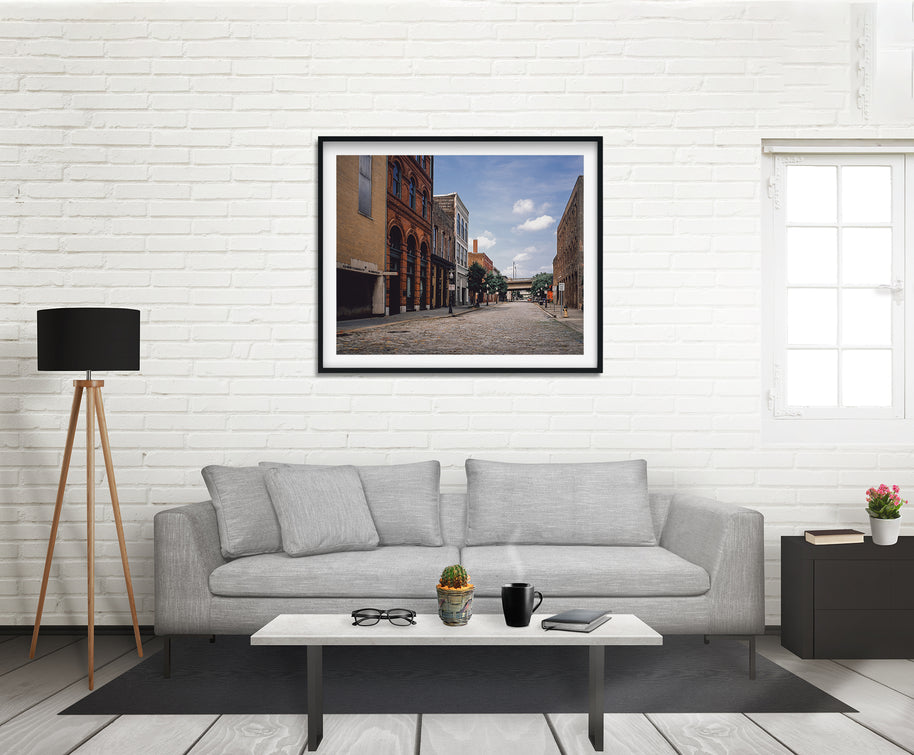 Black-framed brick photo print of a cobblestone street with historic buildings in birmingham alabama under a cloudy sky