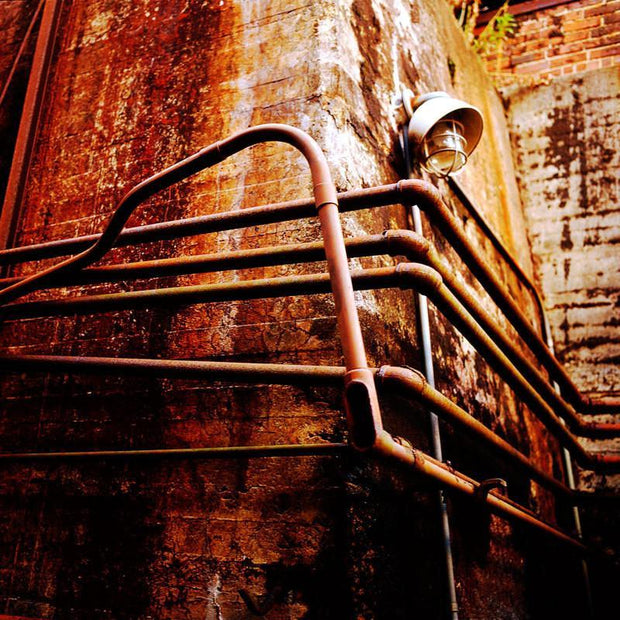 Rusty industrial converging pipes railing with vintage lantern on brick wall in moody industrial photography light leaks