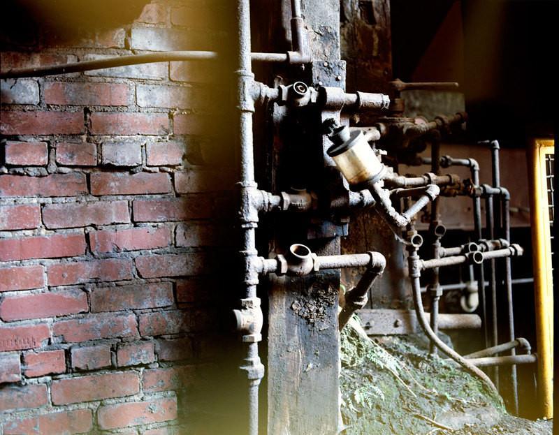Rusty industrial pipe assembly with brass filter in an industrial photography steam photo print featuring bricks and steam