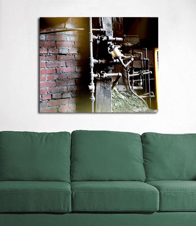 Industrial steam photo print canvas featuring intricate metal pipes and brick wall mounted above green sofa