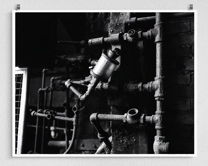 Black-and-white pipe works detail showing industrial pipes and fittings mounted on a brick wall in white industrial photography